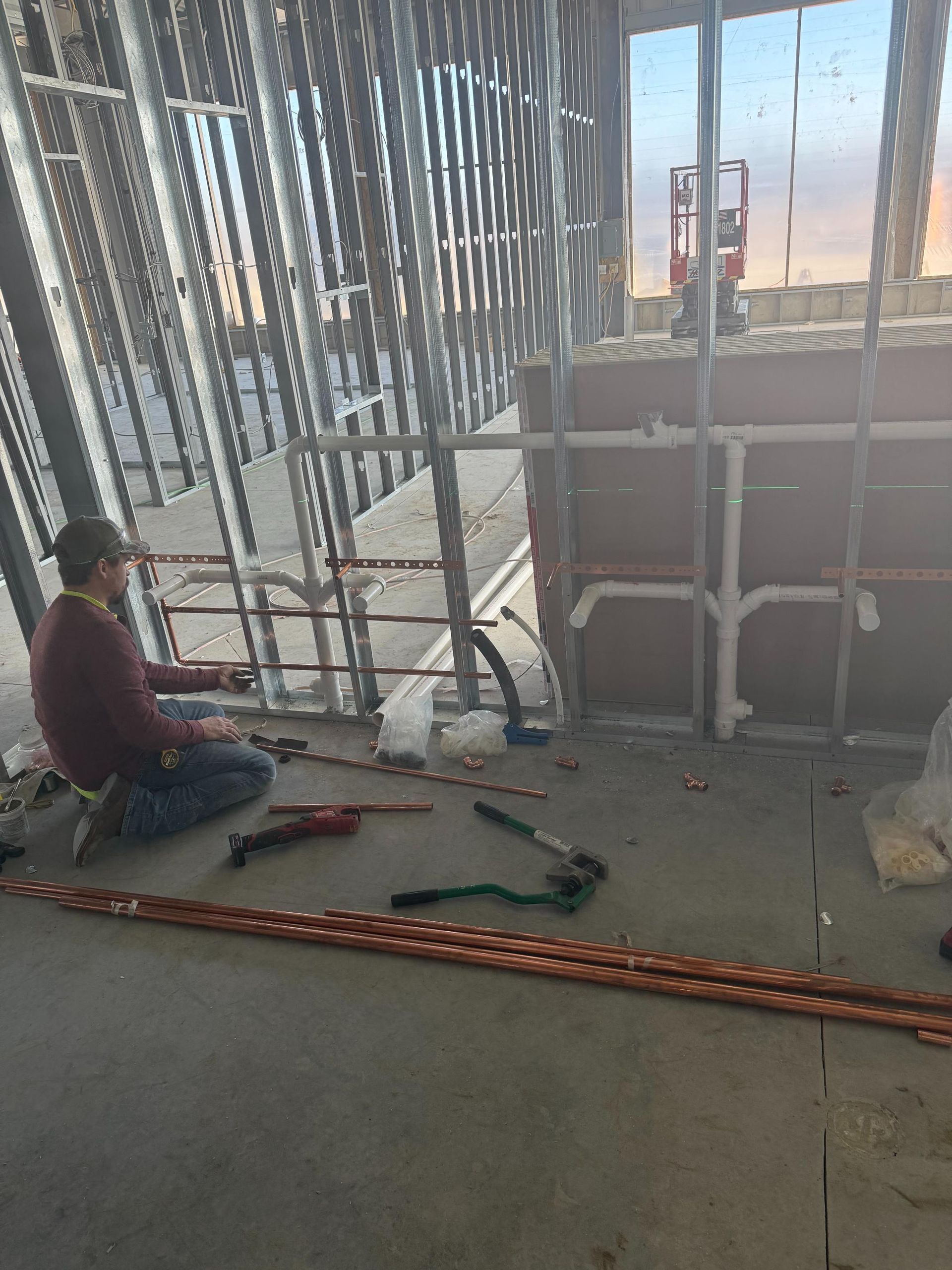 Person kneeling on a construction floor beside tools and metal framing near a large window.