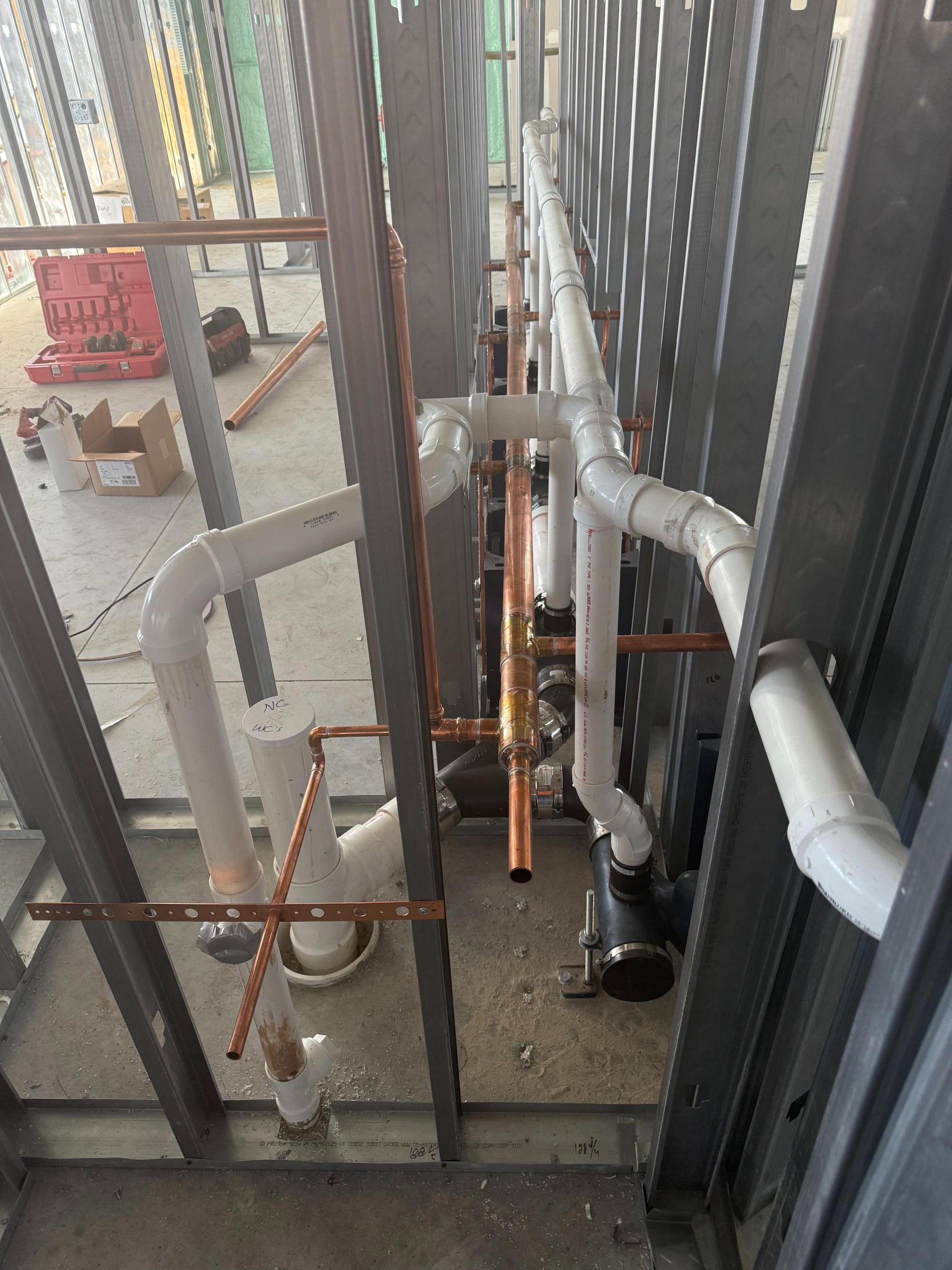 Industrial pipes and cables in a narrow walkway, with metal railings and white PVC piping.