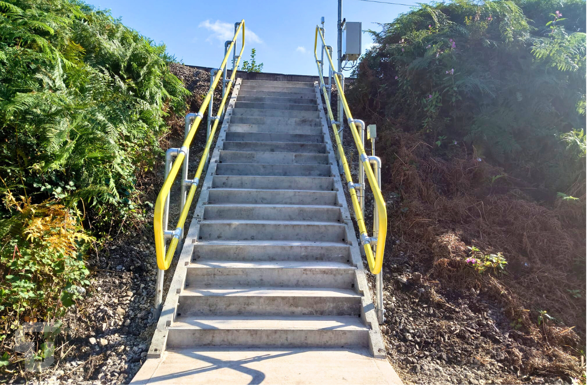 Concrete outdoor stairs with yellow handrails leading up a hillside through greenery