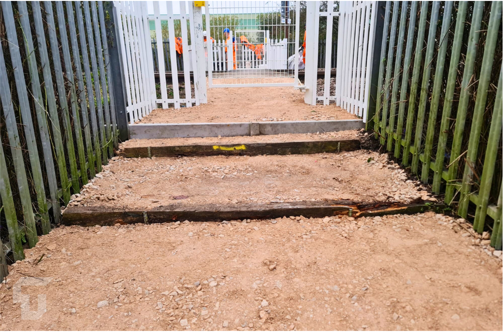 Narrow pedestrian ramp with steps, flanked by black-and-white railings and a gate ahead