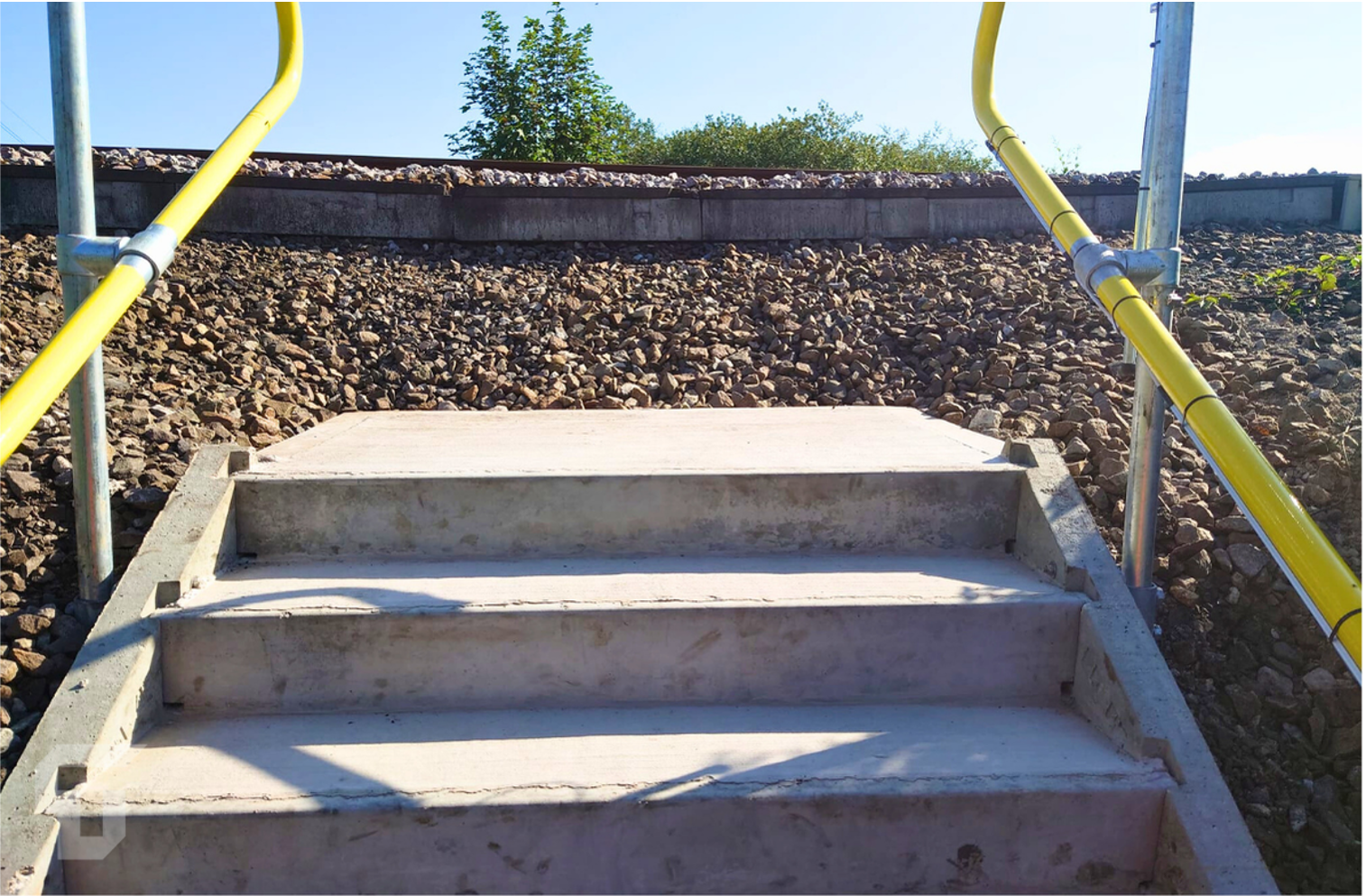 Concrete steps with yellow handrails leading up a stone embankment under a clear sky