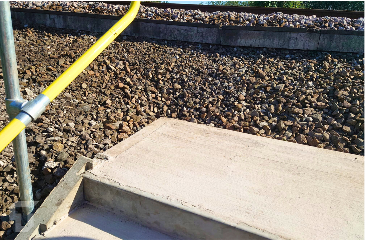 Yellow handrail beside concrete steps and gravel-covered rooftop.