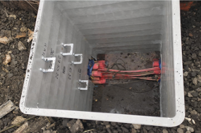 Open utility box with red cables and connectors inside a concrete pit outdoors