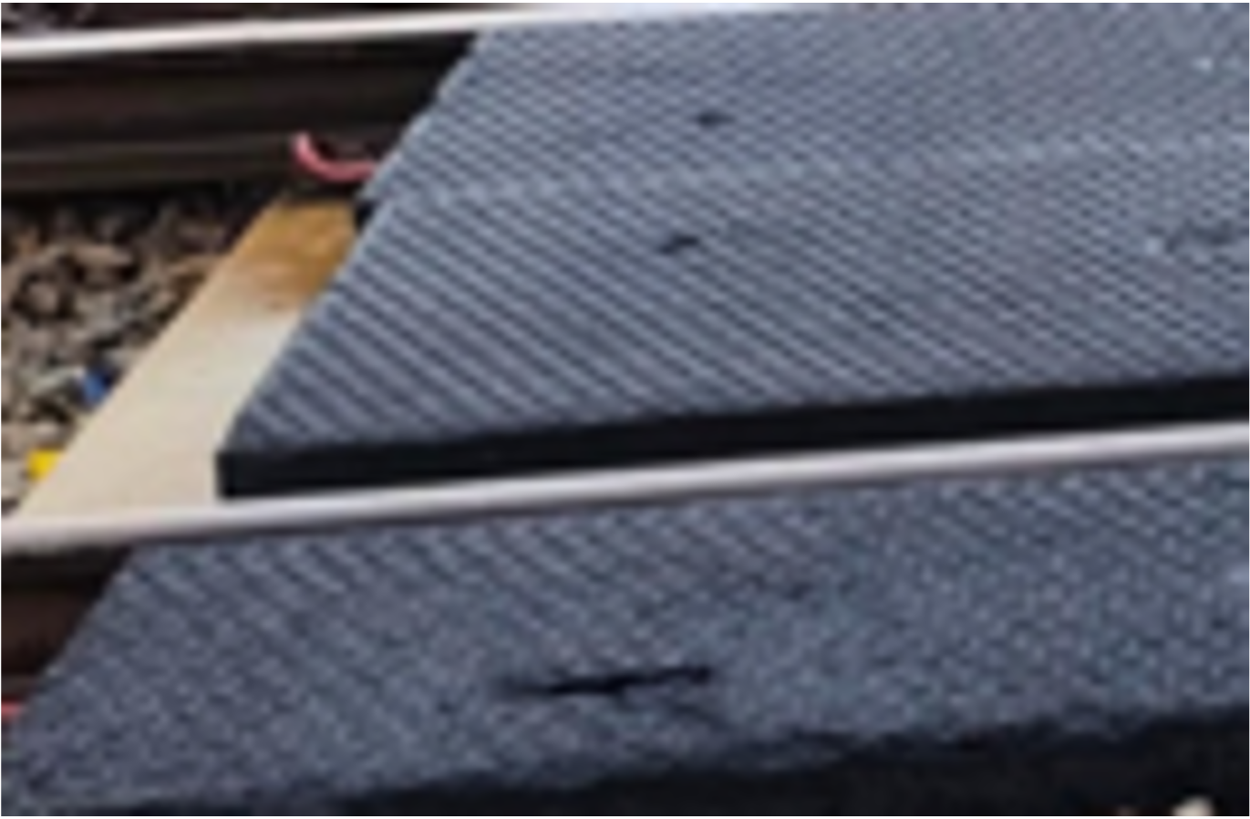 Black ribbed metal ramps beside train tracks with a white rail in front