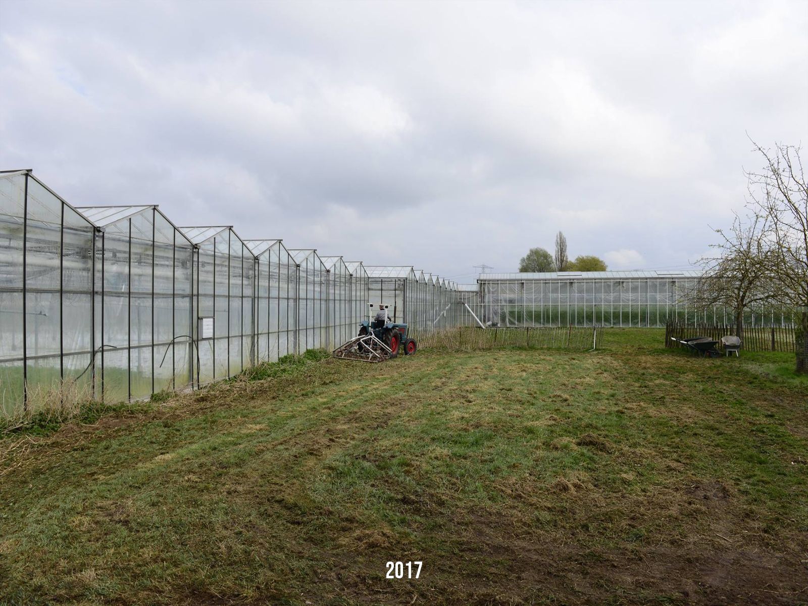 Een man maait het gras in de buurt van kassen op een bewolkte dag.
