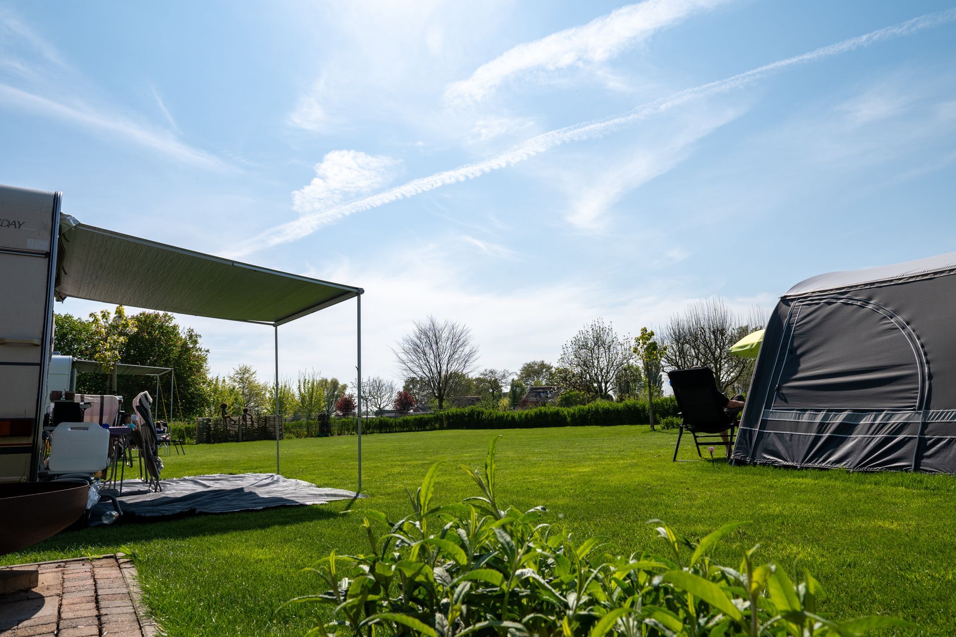 Een kampeertafereel met een caravan en tent op een grasveld onder een zonnige blauwe hemel.