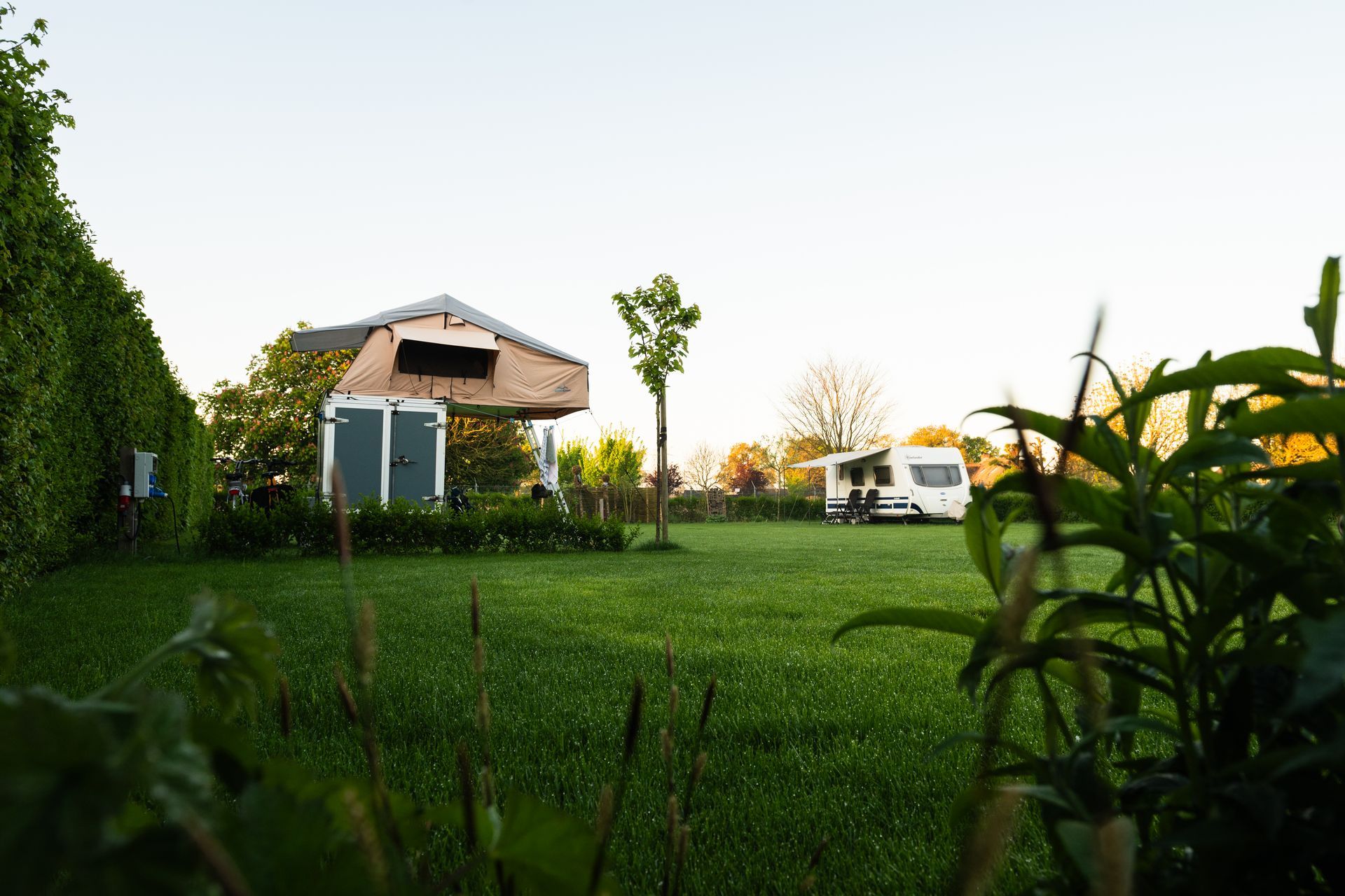 Campingterrein met camperplaats en unieke constructie, groen gazon, bomen en een heldere hemel.