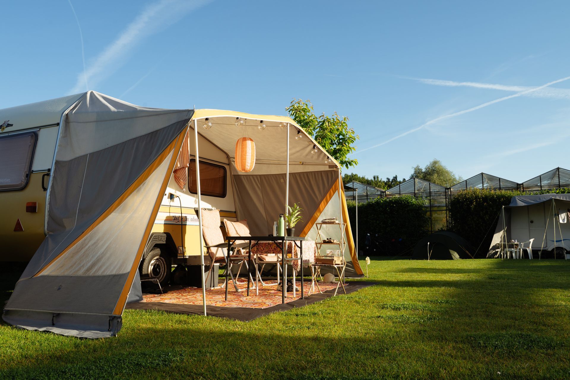 Een camping met een aantal caravans en een tent op een groen gazon onder een blauwe hemel.