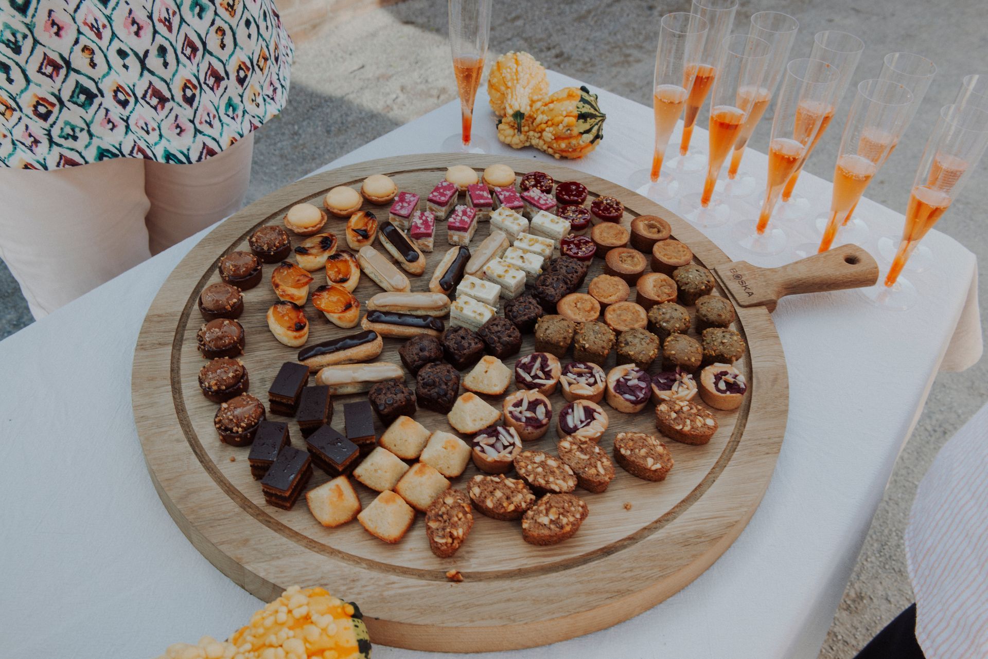 Een houten schaal met diverse gebakjes en champagneglazen op een wit tafelkleed.