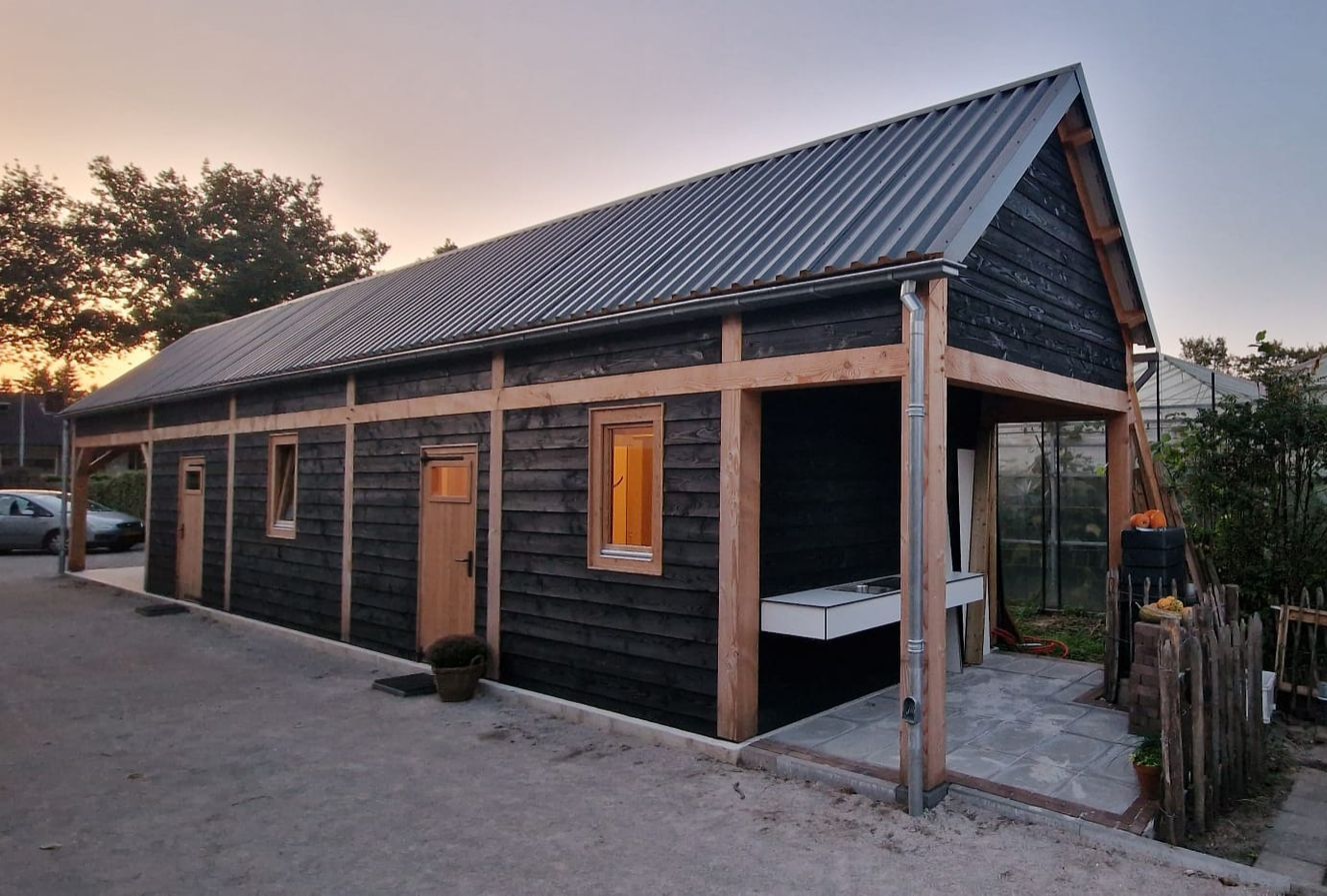 Donker gebeitst houten gebouw met een golfplaten dak en een overdekte veranda.