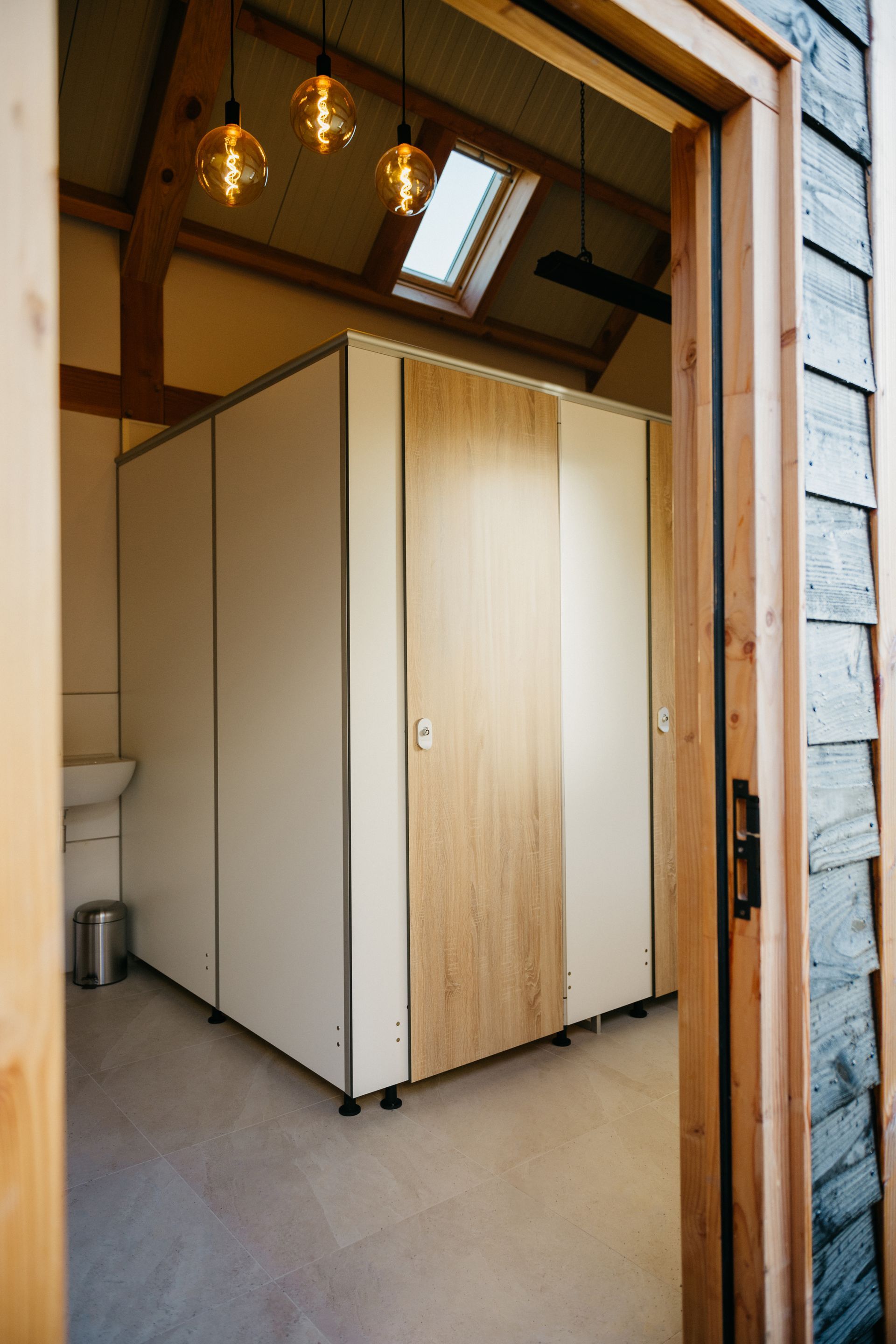 Toiletcabines in een rustieke omgeving, met houten deurkozijn en dakraam erboven.