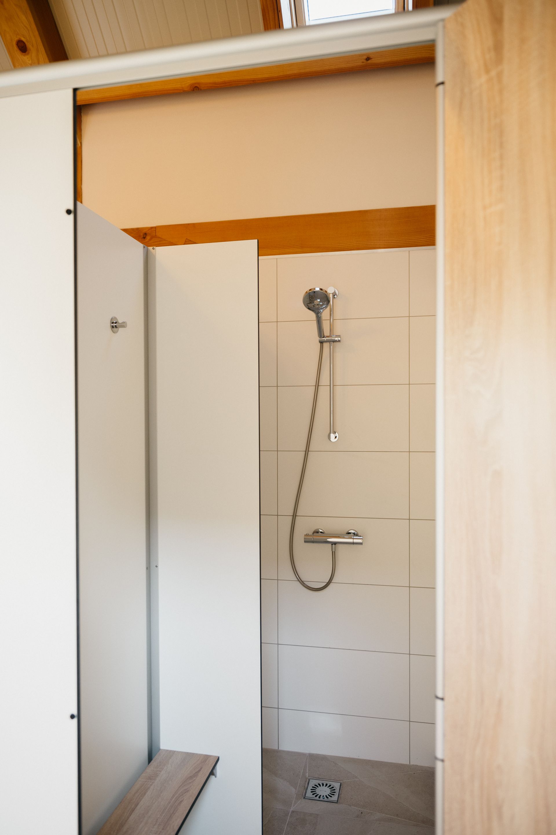 Interieurfoto van een douchecabine met witte muren, een zilverkleurige douchekop en een houten bankje.