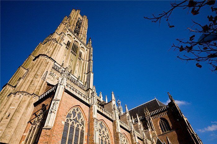 Een laag perspectief van een historische kerktoren Eusebius kerk, in Arnhem, opgetrokken uit lichte steen en rode baksteen, tegen een diepblauwe hemel.