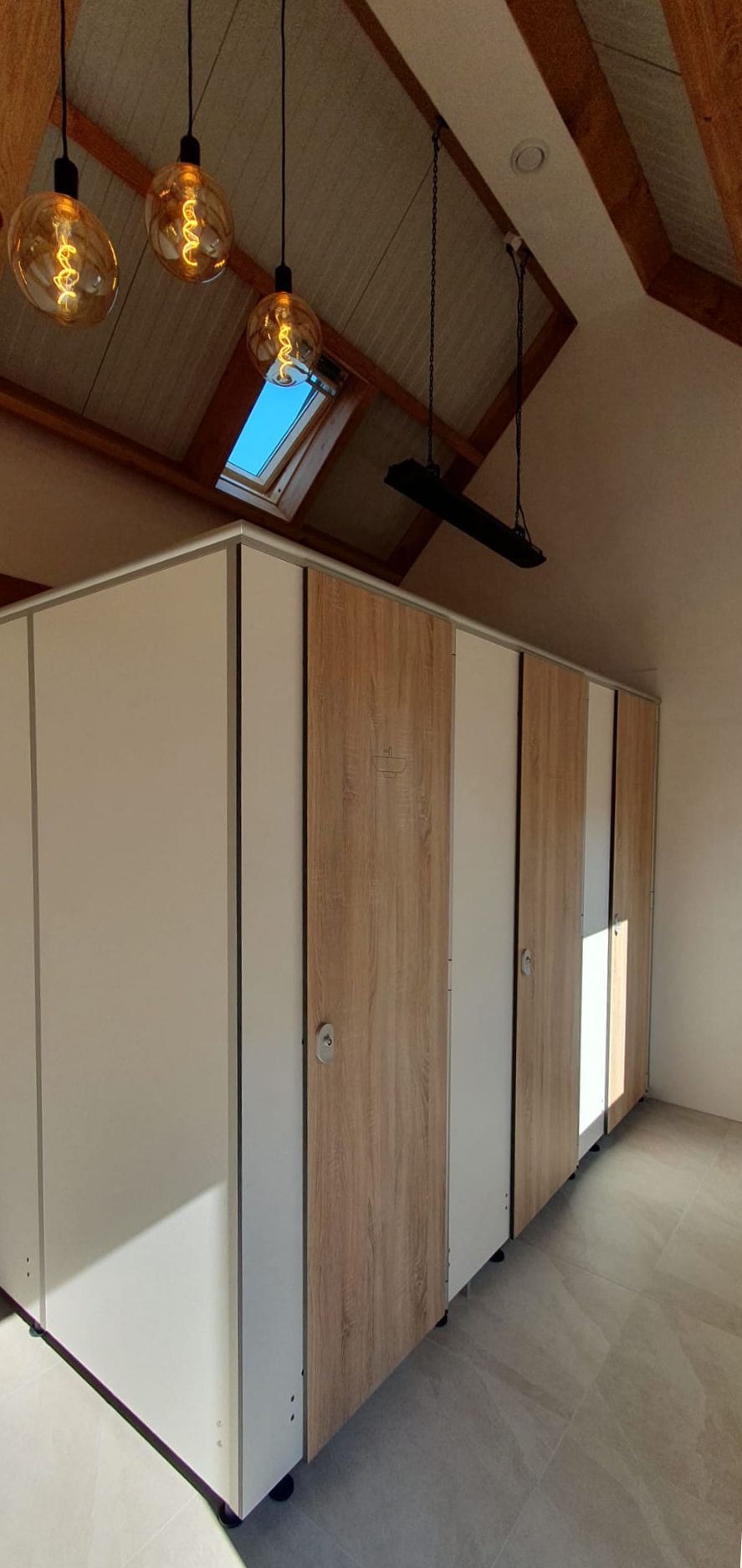 Moderne toiletcabines met houten en witte panelen, een dakraam en hanglampen.