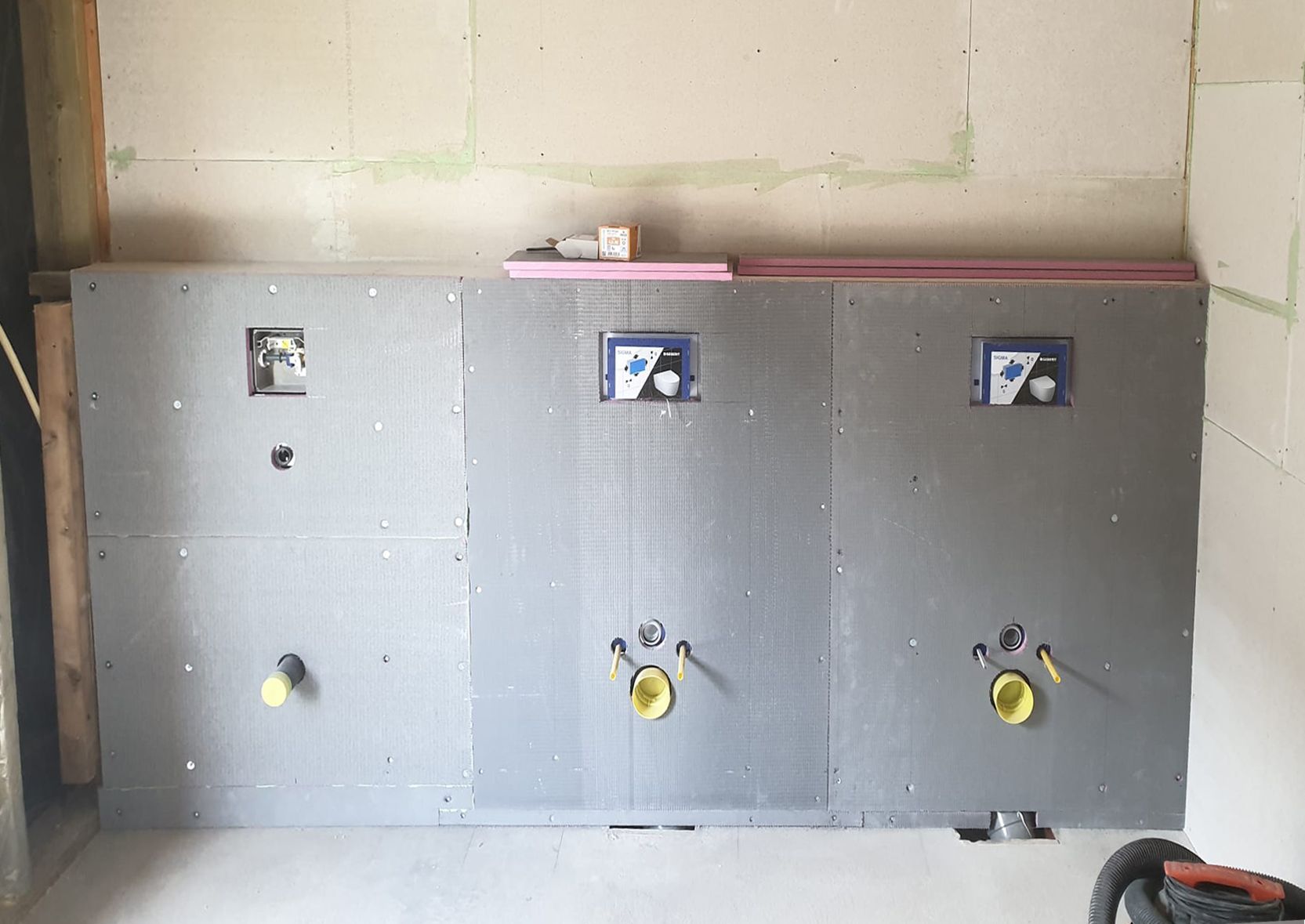 Badkamerwand in aanbouw, met geïnstalleerde sanitaire voorzieningen en grijze wandpanelen.