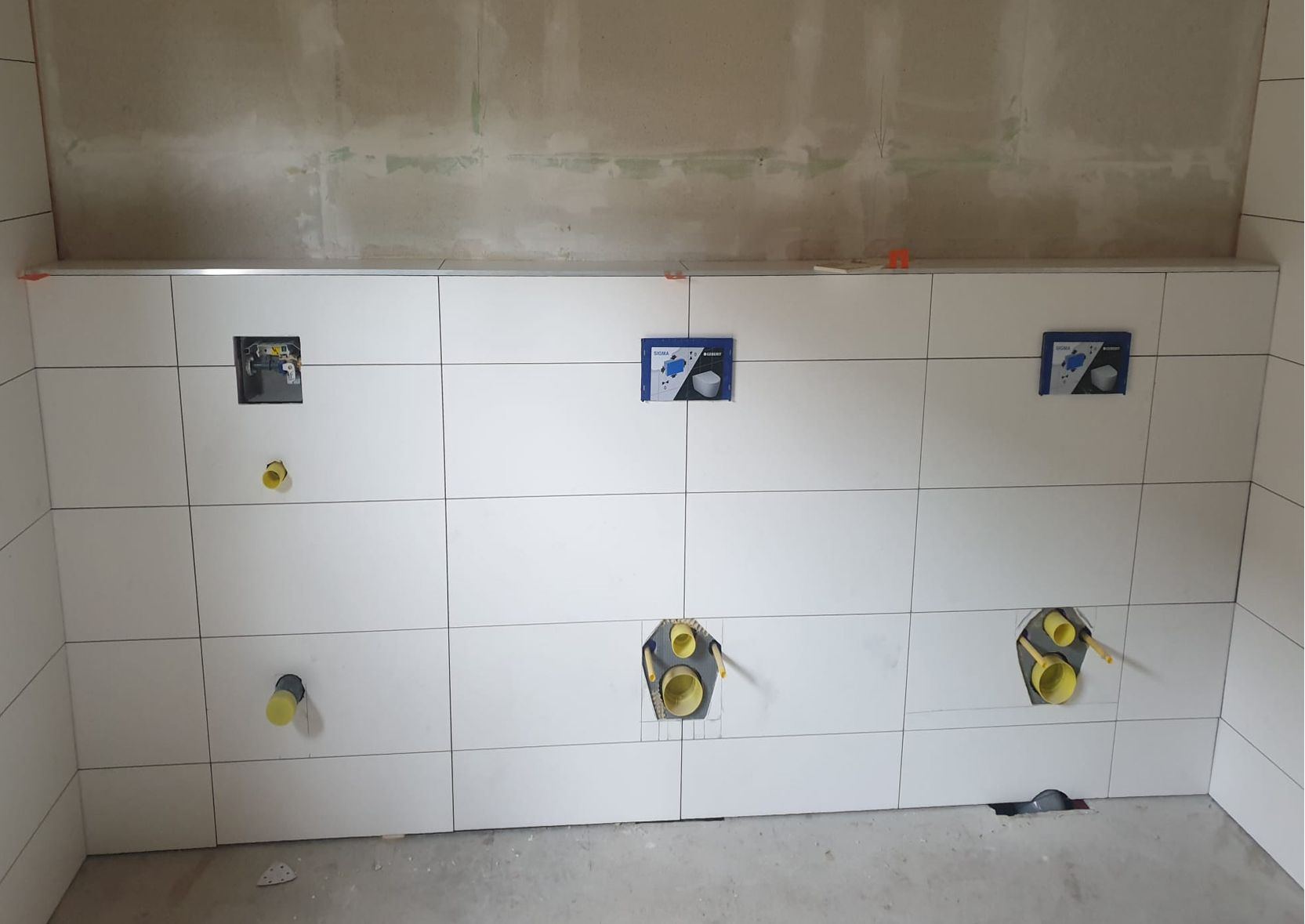 Wandinstallatie met witte tegels en sanitair.
