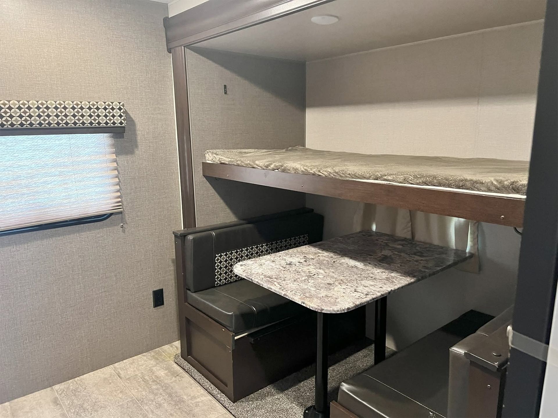 Compact RV sleeping nook with bunk beds, patterned cushions, and a small table by the window.