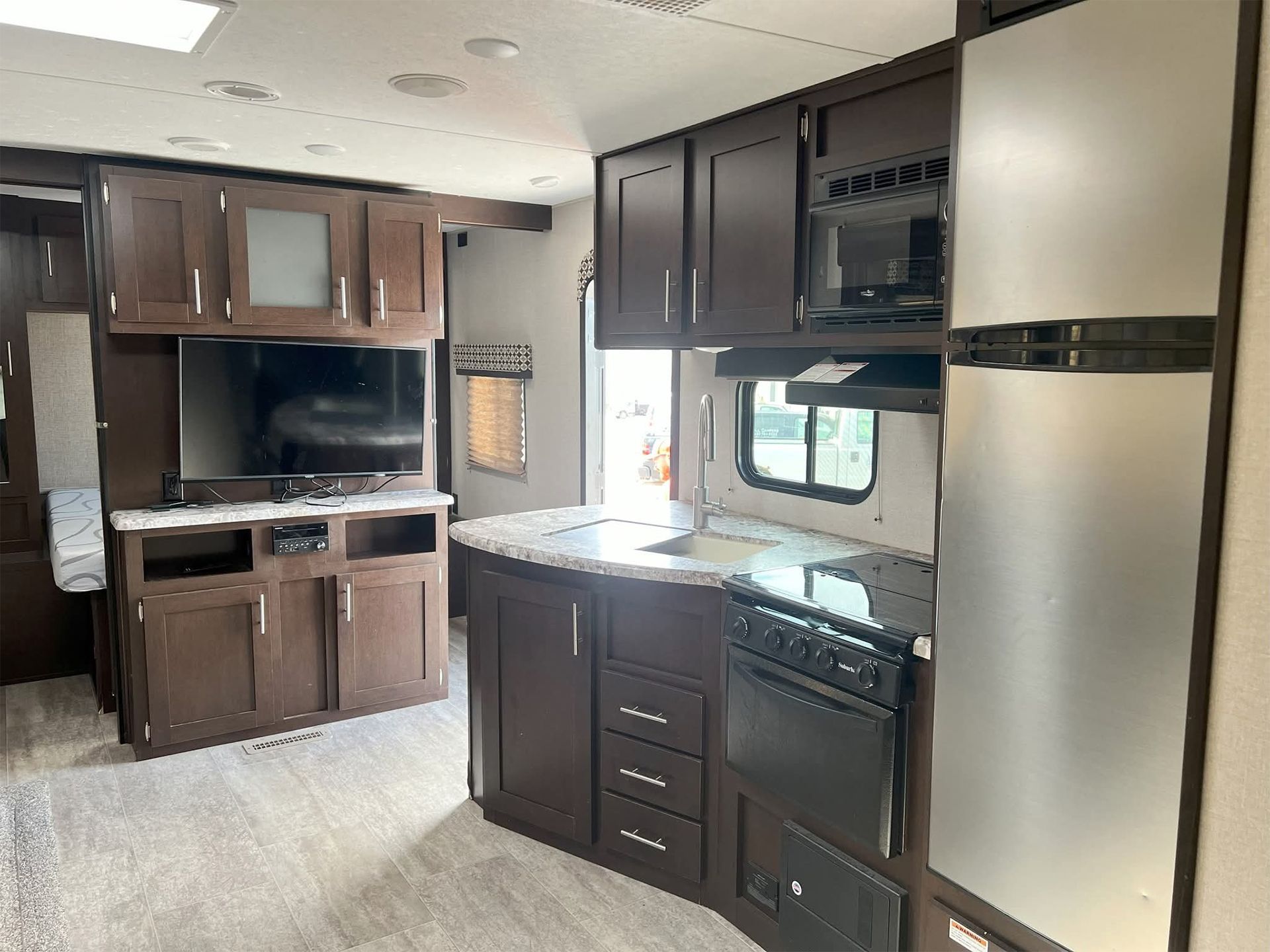 Small RV kitchen with dark wood cabinets, black appliances, and a window over the sink