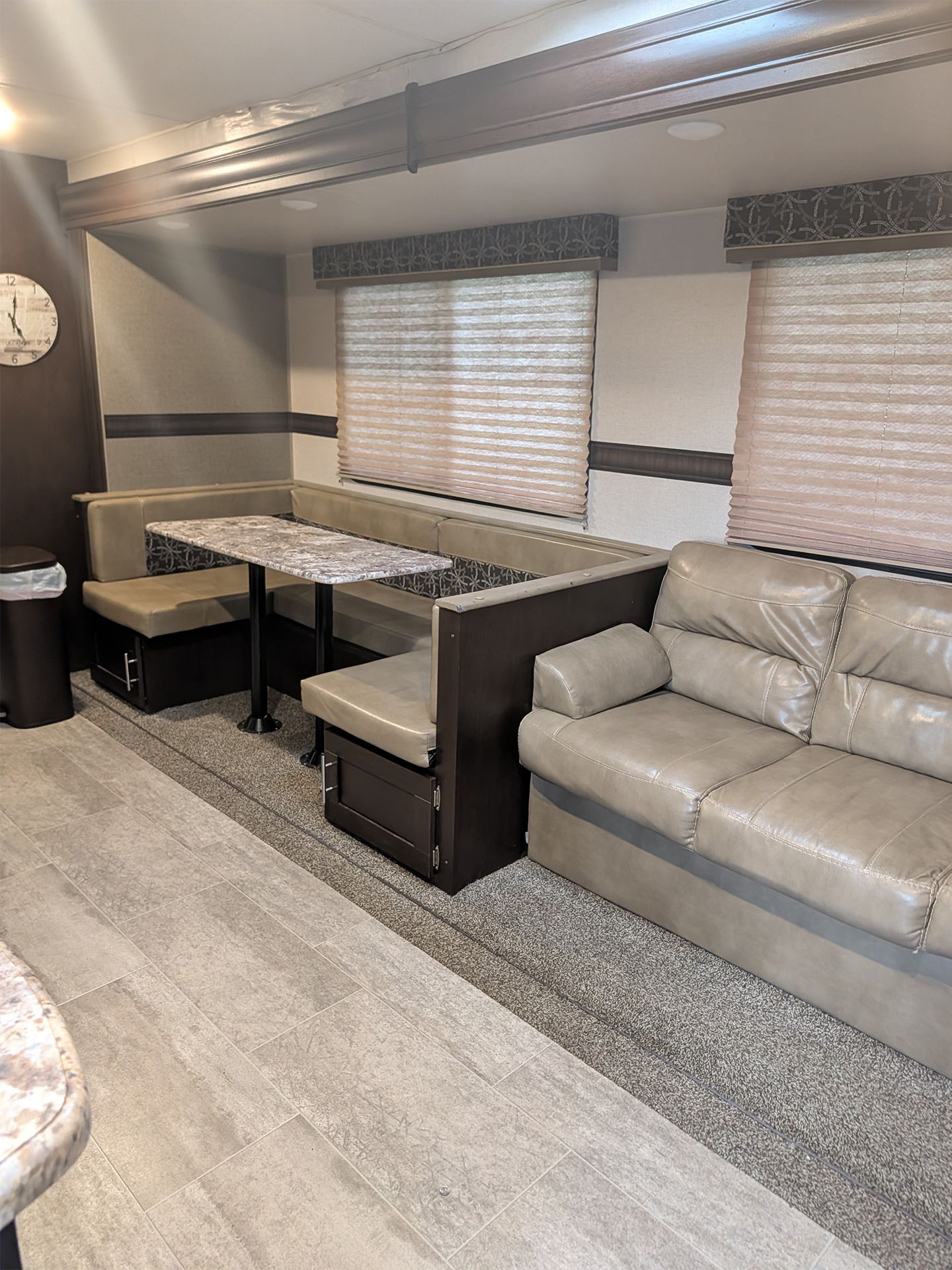 Compact RV living area with beige sofa, booth dining table, and window blinds on gray carpeting