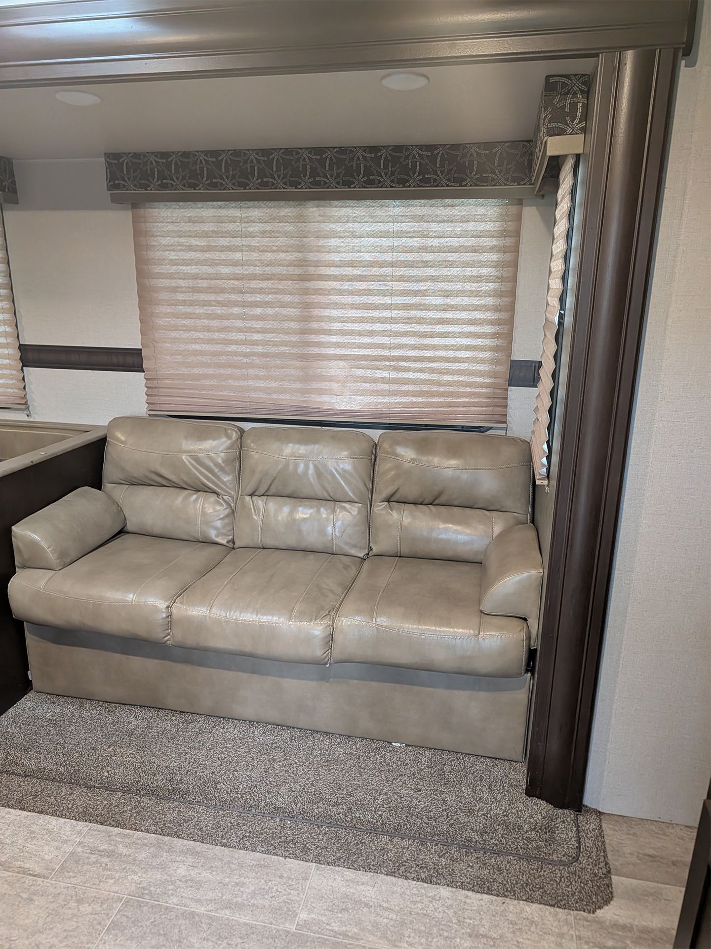 Beige sofa in a small RV living area with window blinds and patterned rug