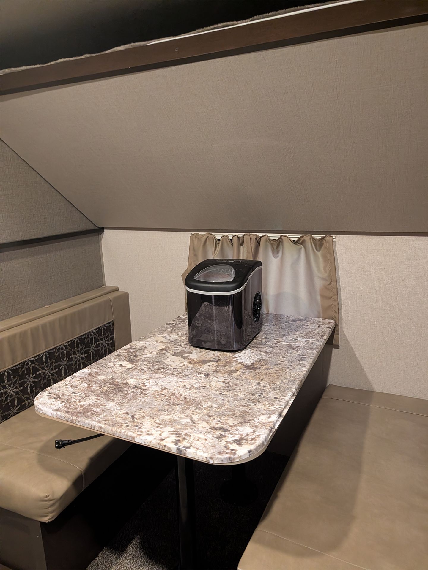 Small attic-style room with a patterned table, bench seating, and a black appliance on the table.