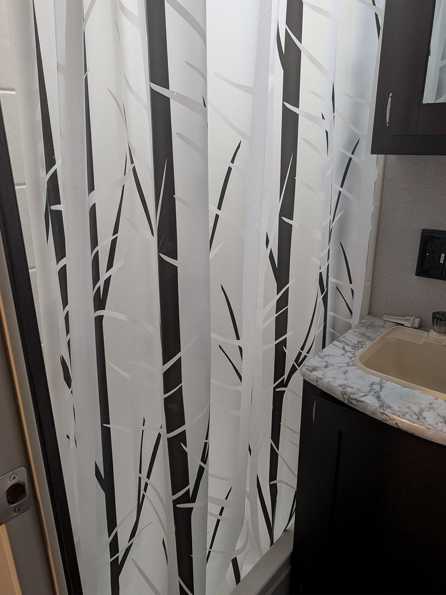 Bathroom with white leaf-pattern shower curtain beside a sink and mirror edge.