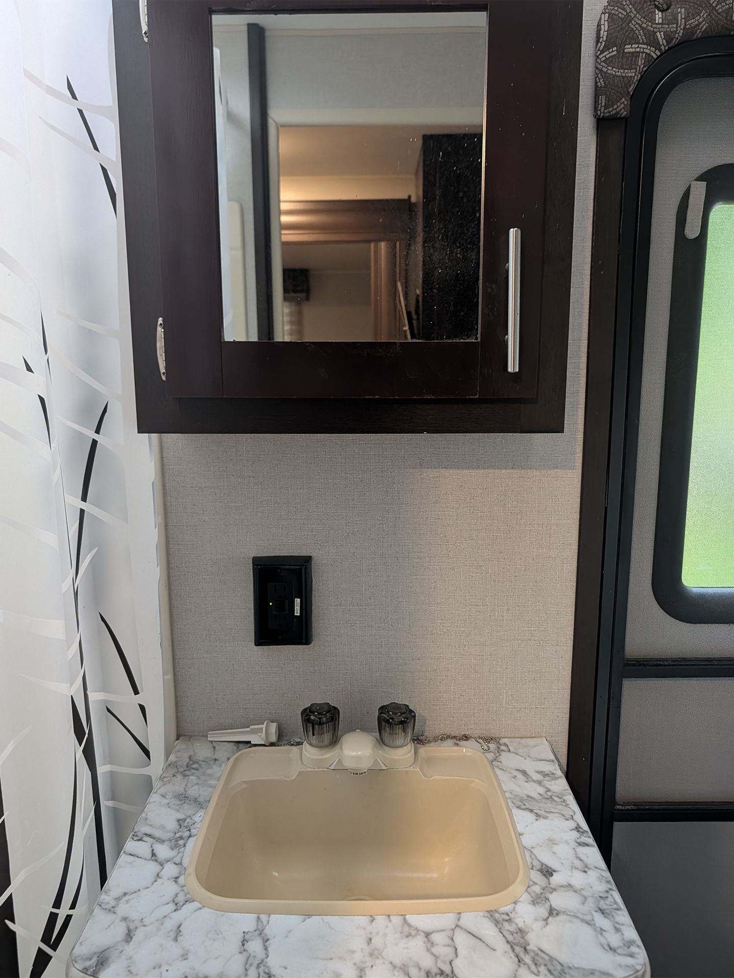 Compact bathroom sink with marble countertop and dark-framed mirror in an RV interior