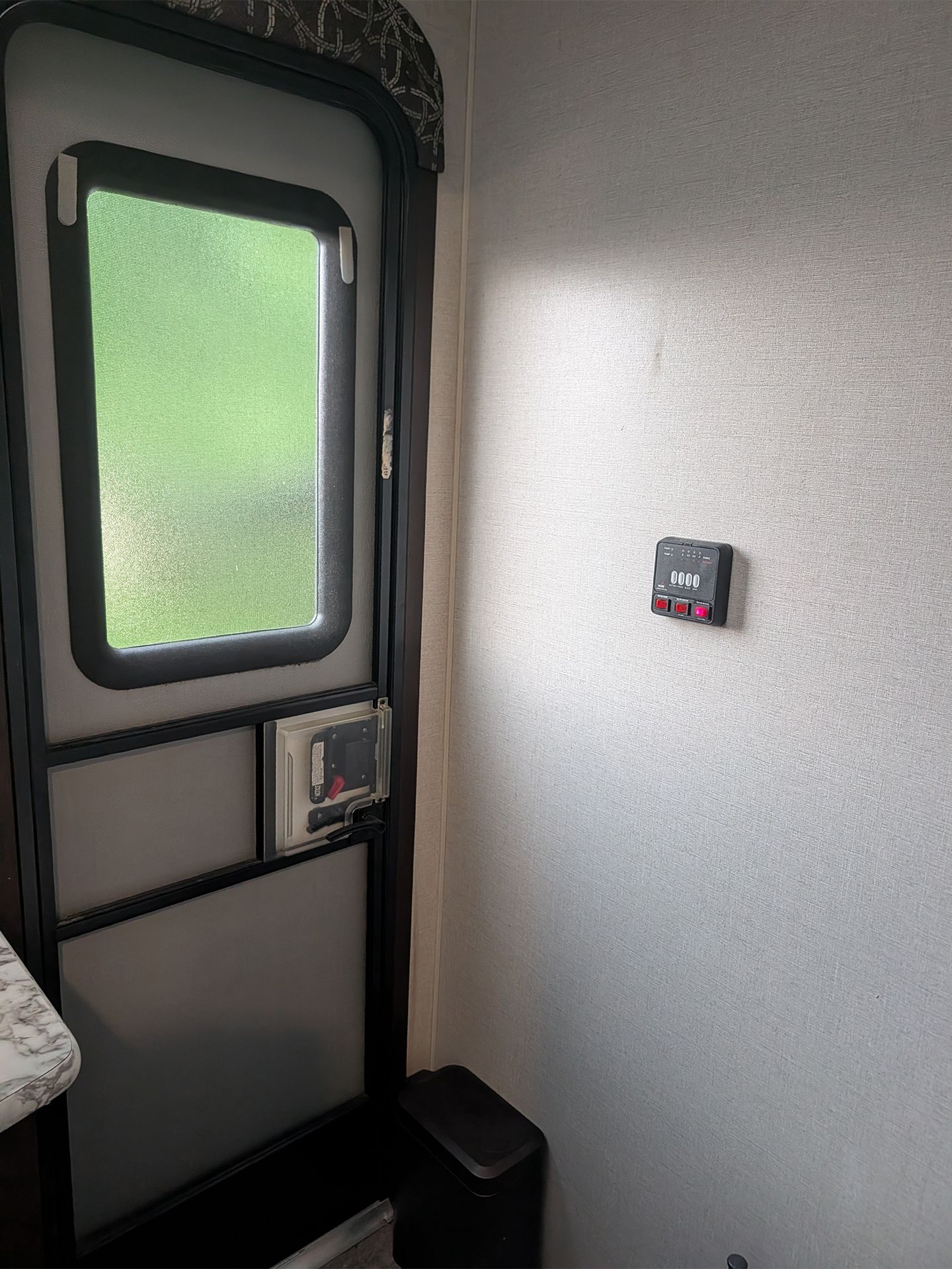 Small RV interior with frosted door window and a wall-mounted switch panel.
