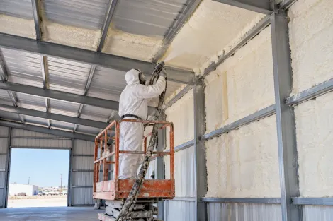 Contractor applying spray foam insulation to metal building walls and ceiling in Odessa, Texas.