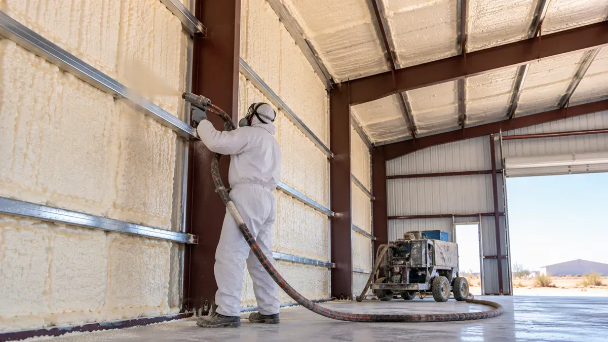 Technician applying spray foam insulation to metal warehouse walls in Odessa, TX.
