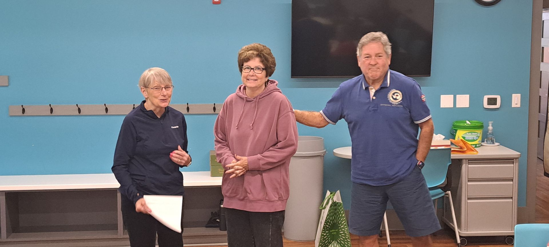 Three people stand in a room with blue walls, two women and one man.