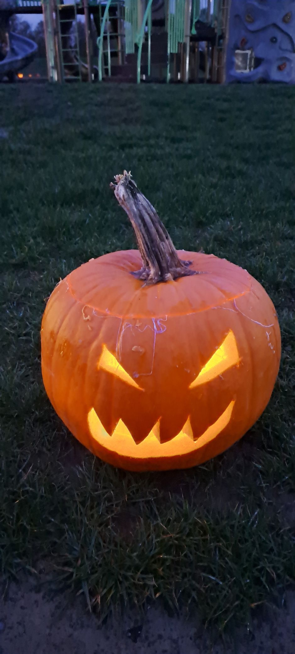 Jack-o'-lantern with glowing face on green grass.