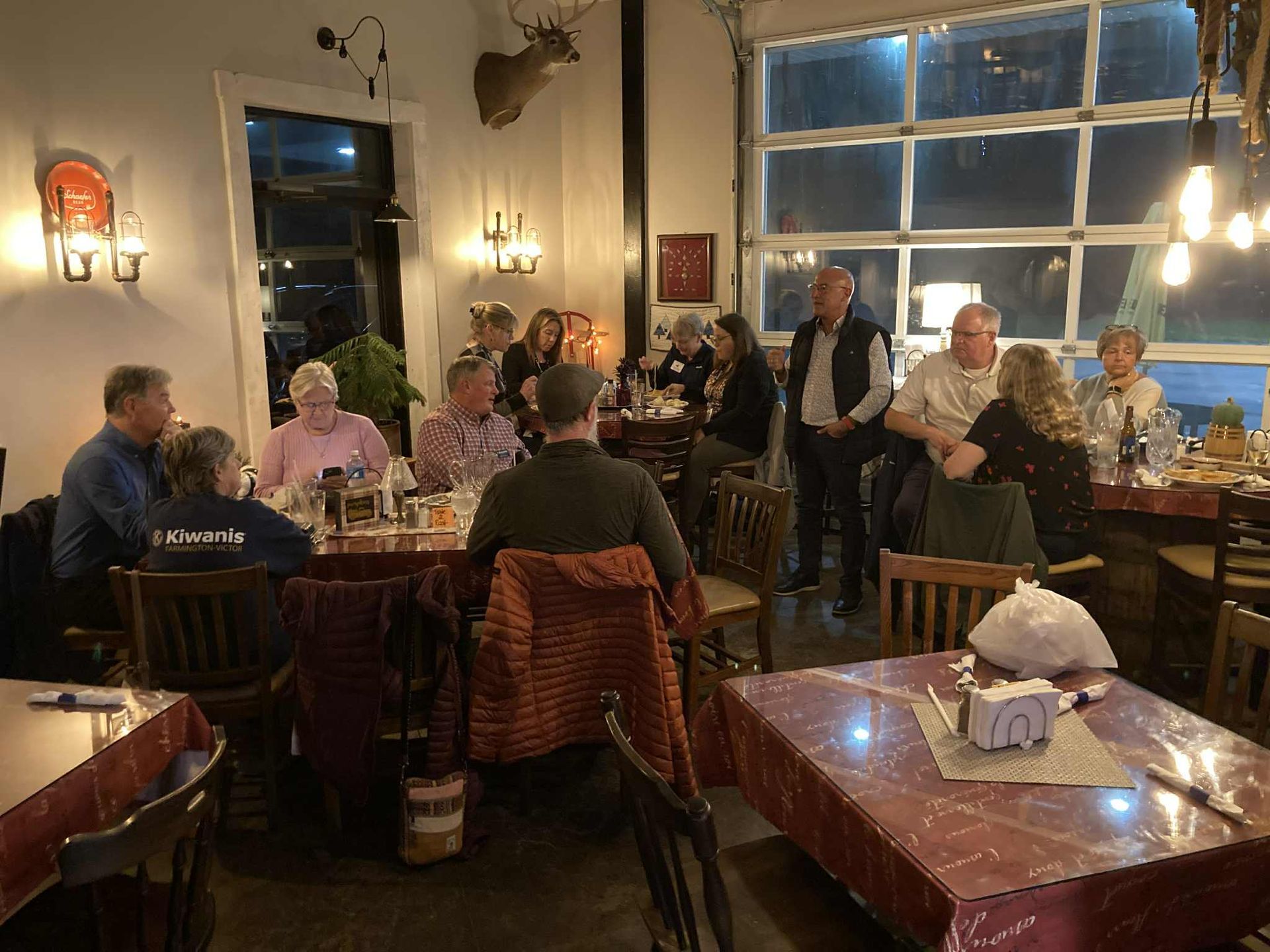 People gathered around tables in a dimly lit restaurant; some are conversing, others are standing.