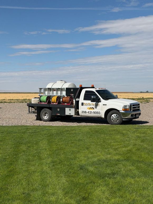 White utility truck with equipment parked beside a gravel road and green field under a blue sky
