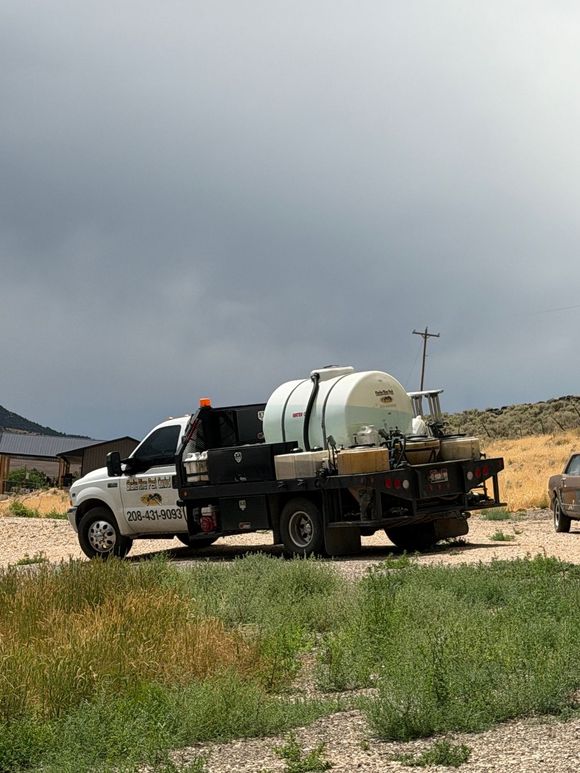 White utility truck with a large tank parked on a dirt road under cloudy skies.