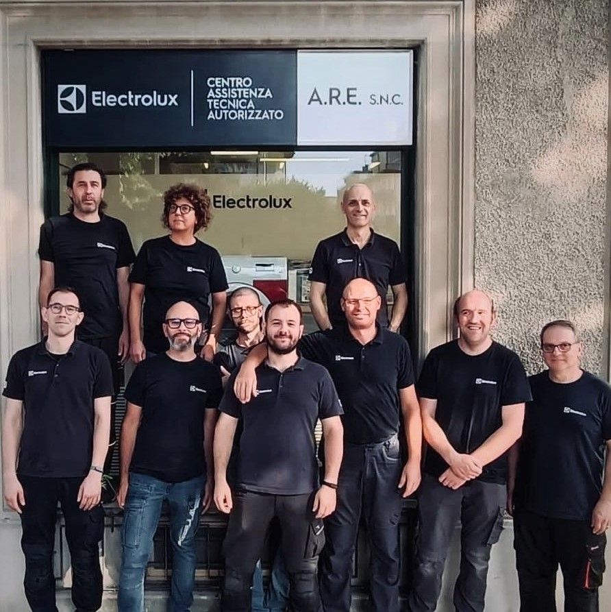Il team di assistenza Electrolux posa davanti a un negozio, con l'insegna dell'azienda sopra di loro.