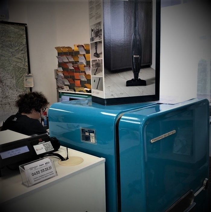 Una persona lavora accanto a un frigorifero retrò blu lucido in un piccolo negozio o ufficio.
