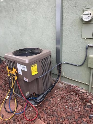 Outdoor HVAC unit with gauges and hoses beside a house wall and utility meter