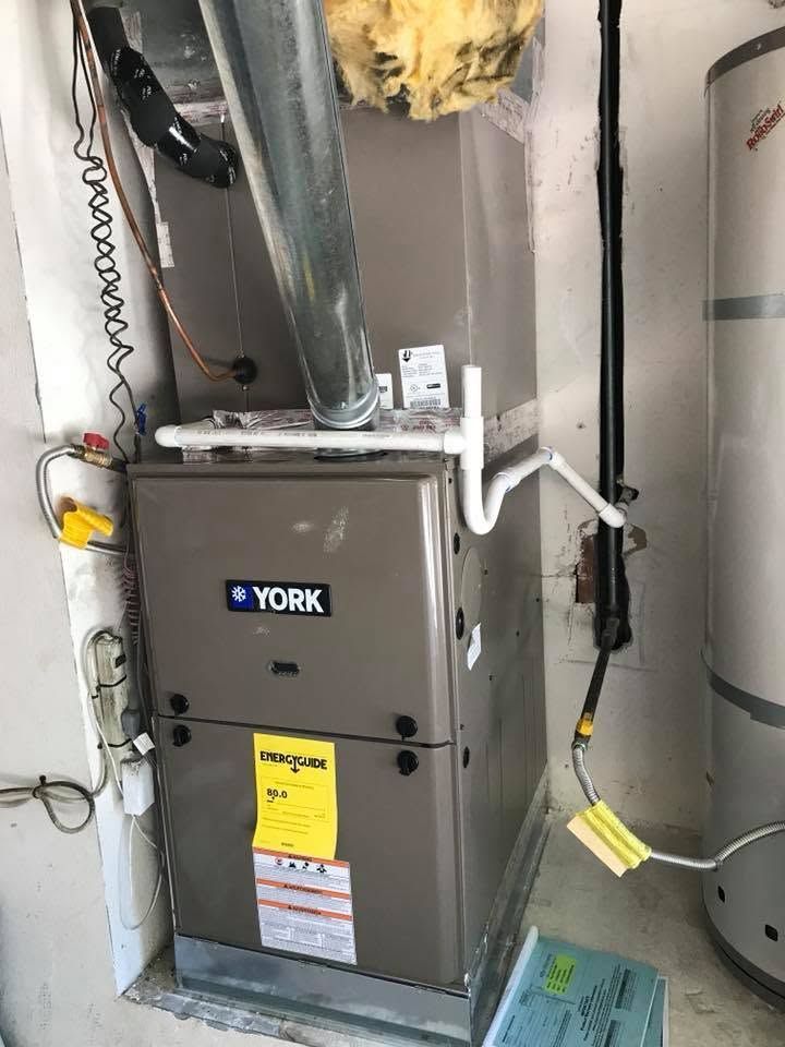 York furnace in a utility closet with metal ductwork and nearby water heater.