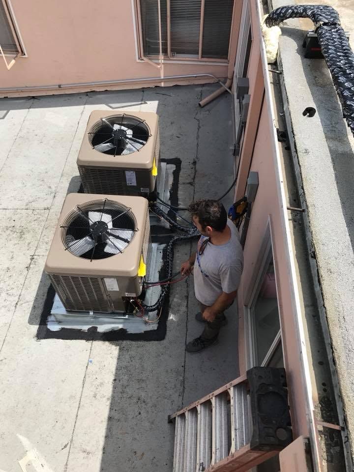 Two rooftop AC units beside a person inspecting equipment on a narrow building roof.
