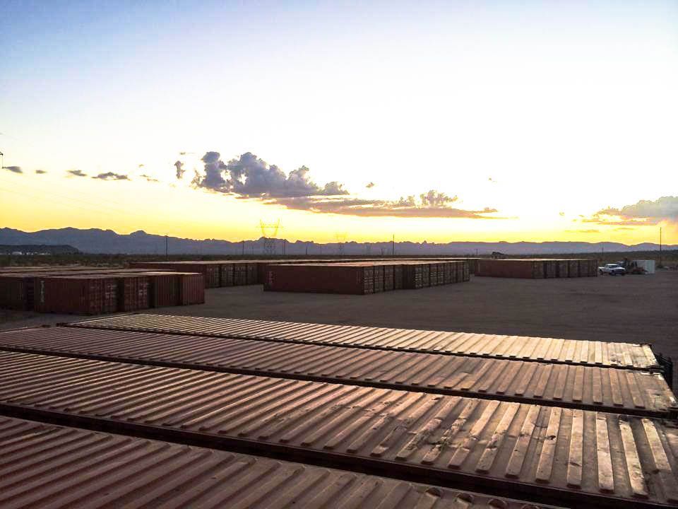 A row of shipping containers are lined up in a field at sunset.