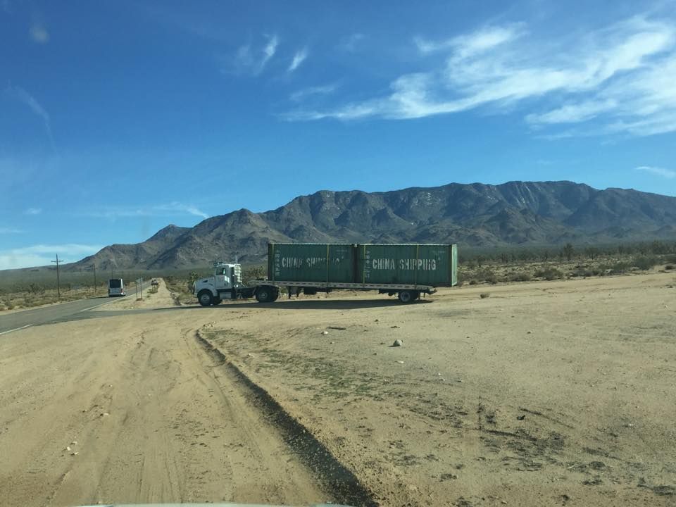 A truck is driving down a dirt road with mountains in the background