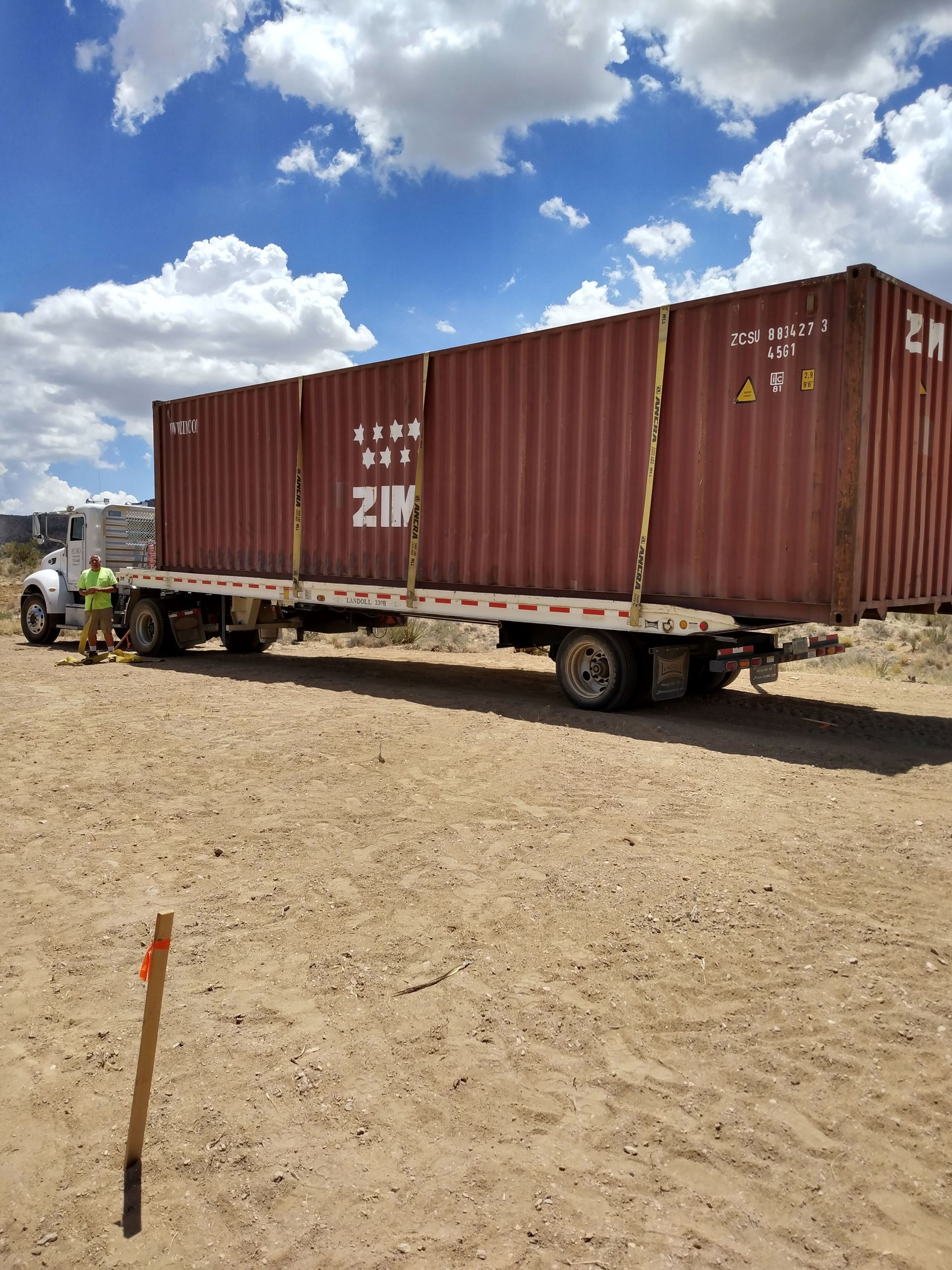 A large shipping container is on a trailer in a dirt field.