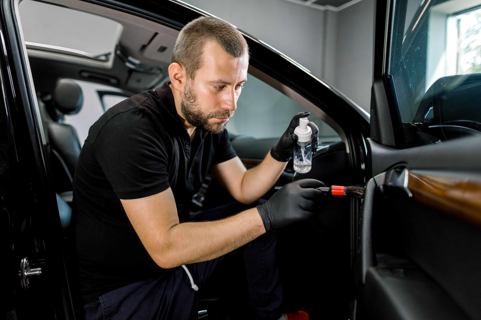 Detailer cleaning a car interior with a spray bottle and cloth in a garage