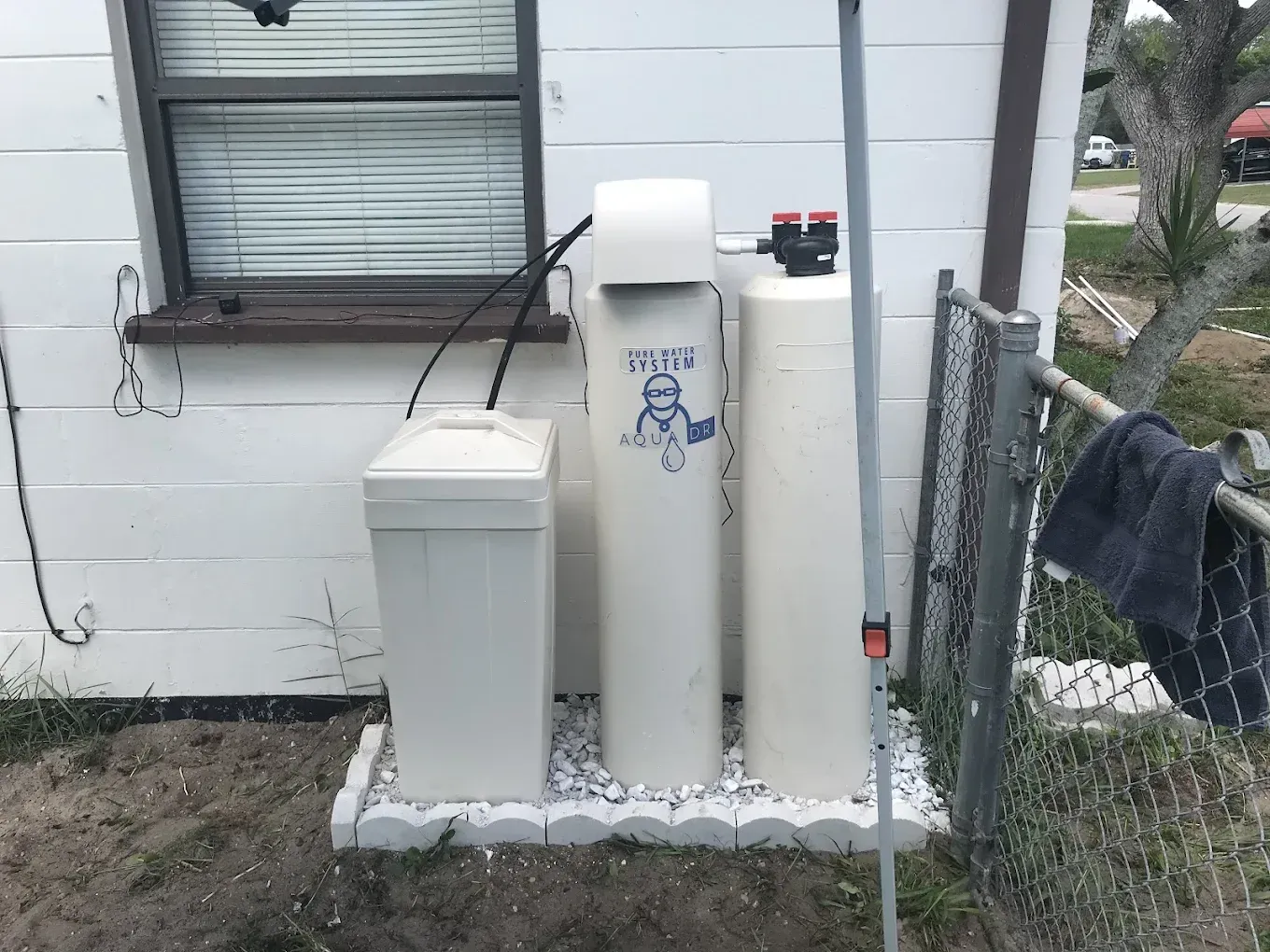 Water softener system installed outside a building next to a window and fence.
