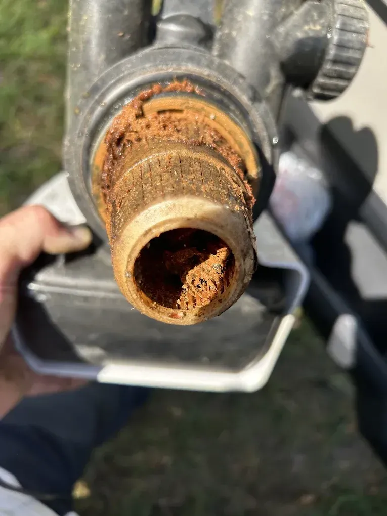 Corroded pipe fitting, showing rust-colored mineral buildup inside a plastic water filter component, held in a hand.