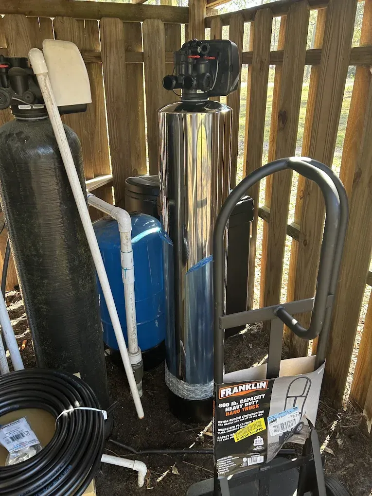 Water filtration system with tanks, piping, and hand truck in a wooden enclosure.