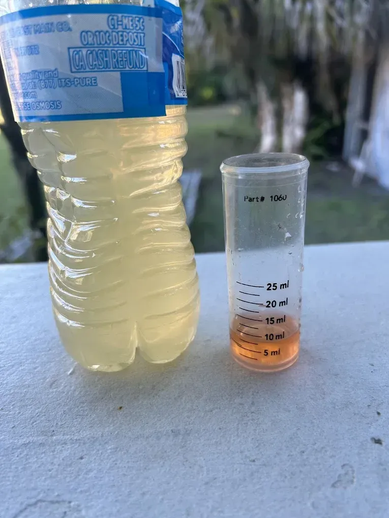 A clear plastic bottle and a test tube with orange liquid on a white surface outdoors.