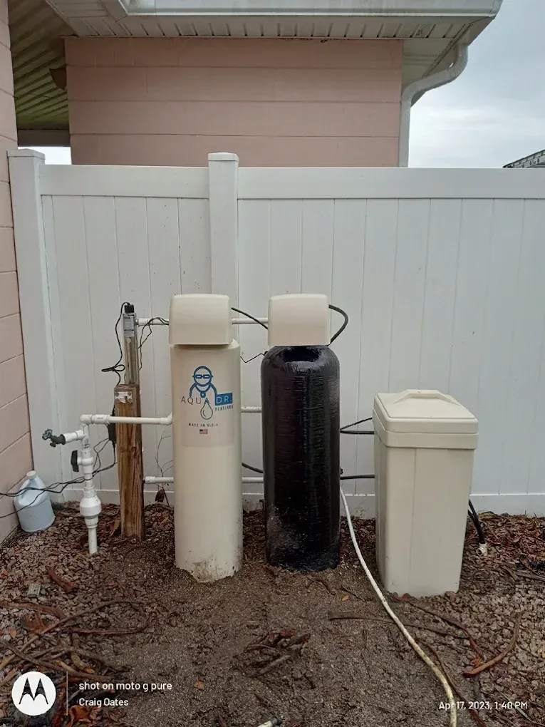 Outdoor water filtration system next to a white fence and a pink wall. Includes two tanks and a salt container.