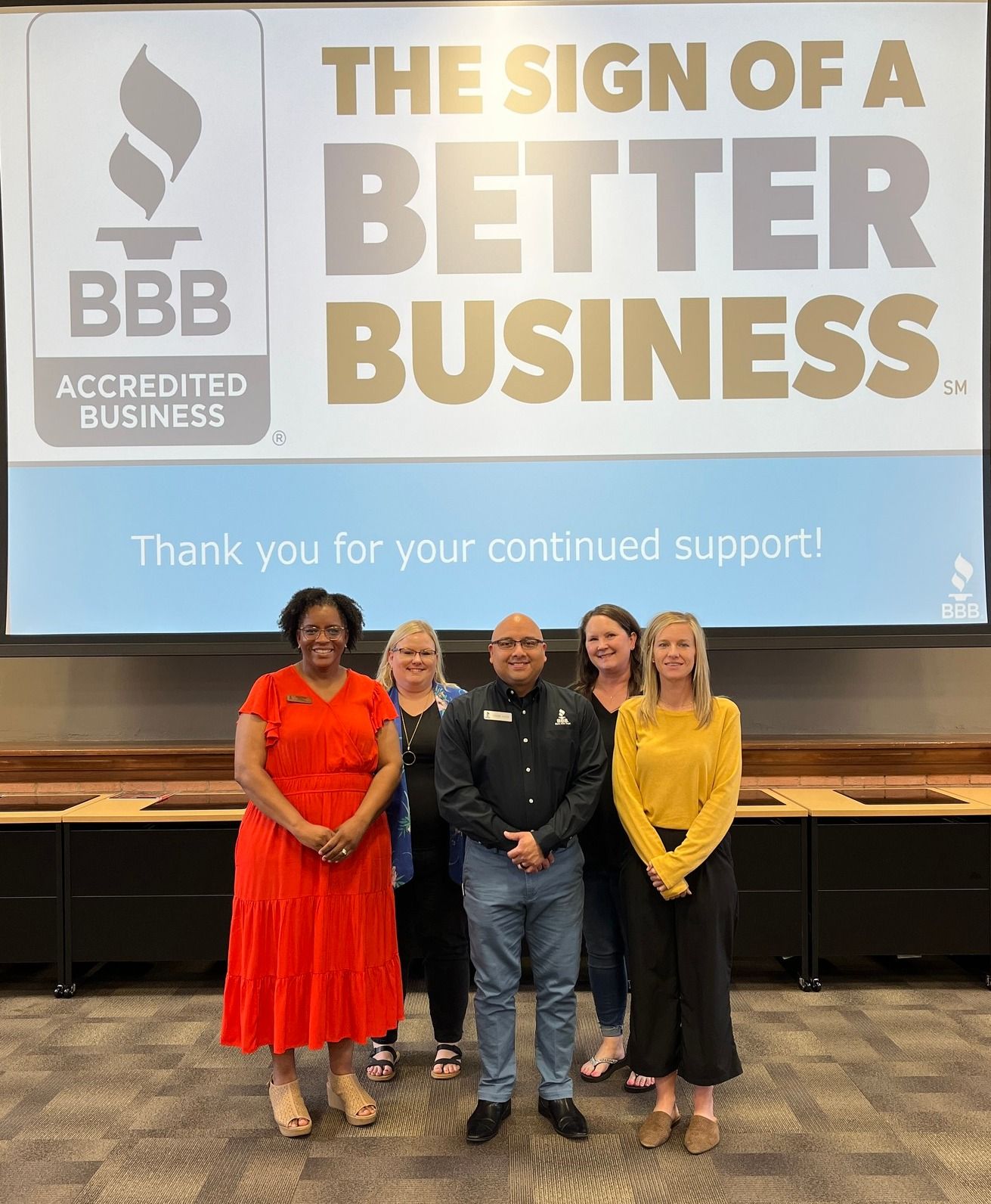 Group of five people standing in front of a screen with a BBB logo and text,